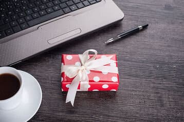 Laptop computer with cup of tea and gift box - Employee Compensation - BizEdge blog