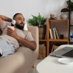 a man spending his time off at home watching a movie and holding a cup of coffee.