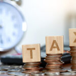 TAX blocks on coin stacks with a clock in the background - 16 New Changes in Nigeria’s 2025 Tax Reform Explained - BizEdge blg
