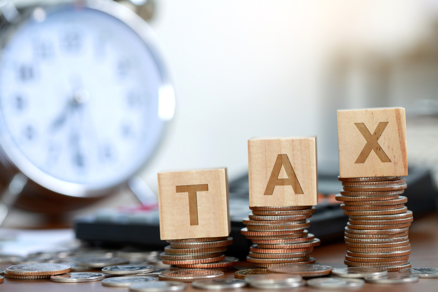TAX blocks on coin stacks with a clock in the background - 16 New Changes in Nigeria’s 2025 Tax Reform Explained - BizEdge blg