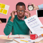 A man surrounded with gadgets and papers - How Busy Teams Can Master Task Prioritization in Simple Steps - BizEdge blog