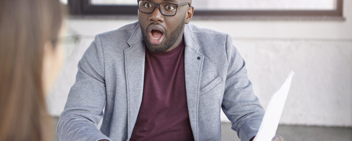 a man looking at a woman surprised with the data on the paper he is holding - performance review biases - BizEdge blog