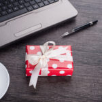 Laptop computer with cup of tea and gift box - Employee Compensation - BizEdge blog