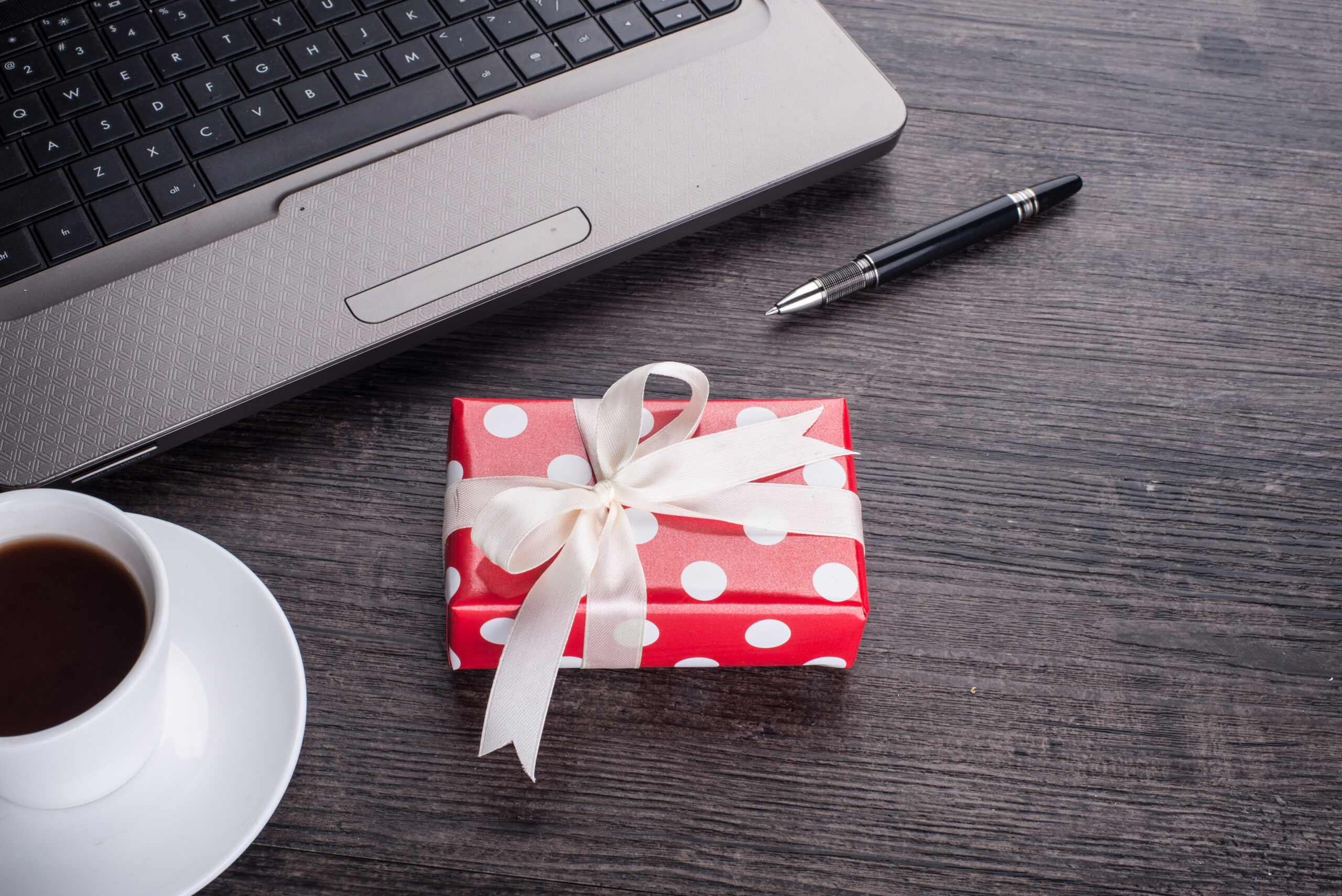 Laptop computer with cup of tea and gift box - Employee Compensation - BizEdge blog