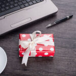 Laptop computer with cup of tea and gift box - Employee Compensation - BizEdge blog