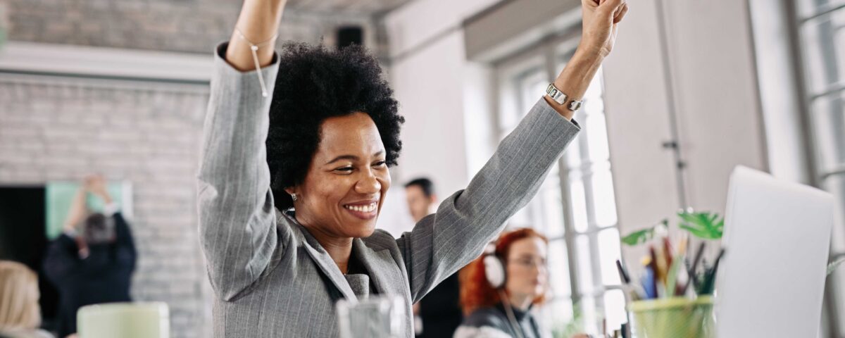 a woman looking at her system excited with her arms raised - 13th month salary - BizEdge blog