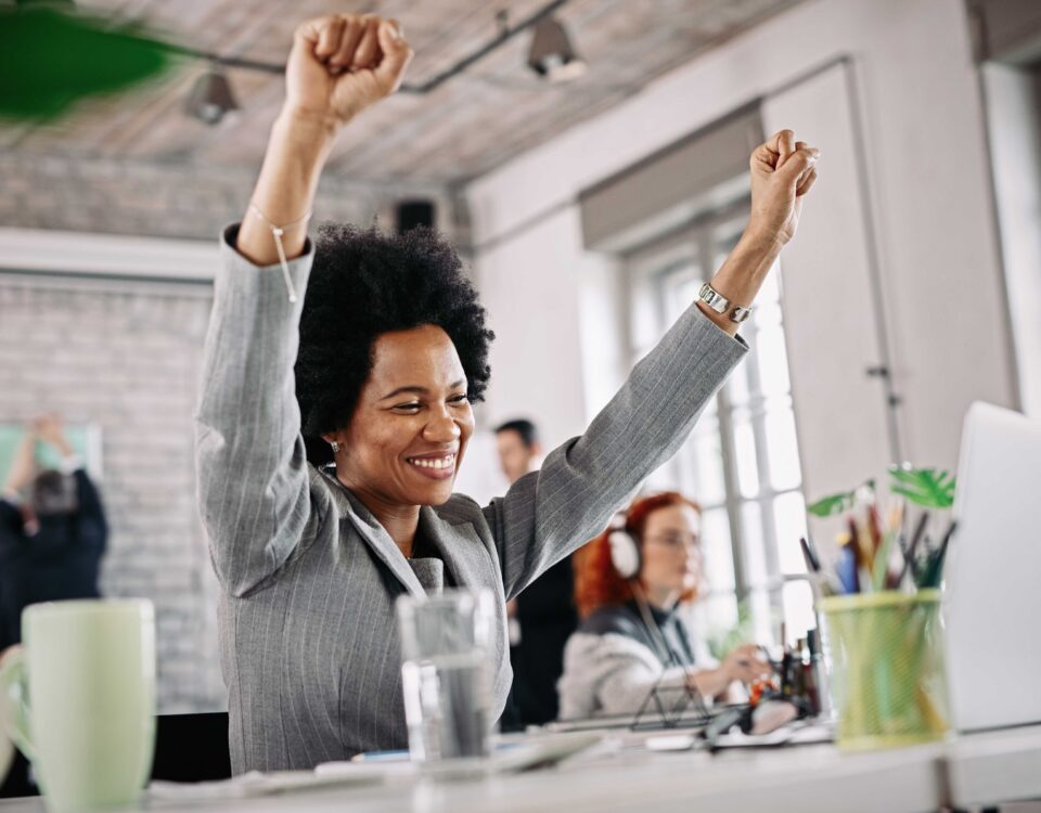 a woman looking at her system excited with her arms raised - 13th month salary - BizEdge blog