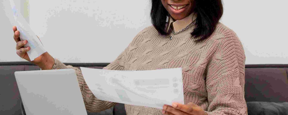 a woman with her laptop on her lap while looking at a document - File Tax in Nigeria - BizEdge blog