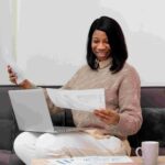 a woman with her laptop on her lap while looking at a document - File Tax in Nigeria - BizEdge blog