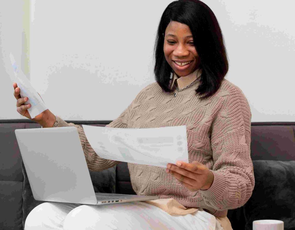 a woman with her laptop on her lap while looking at a document - File Tax in Nigeria - BizEdge blog