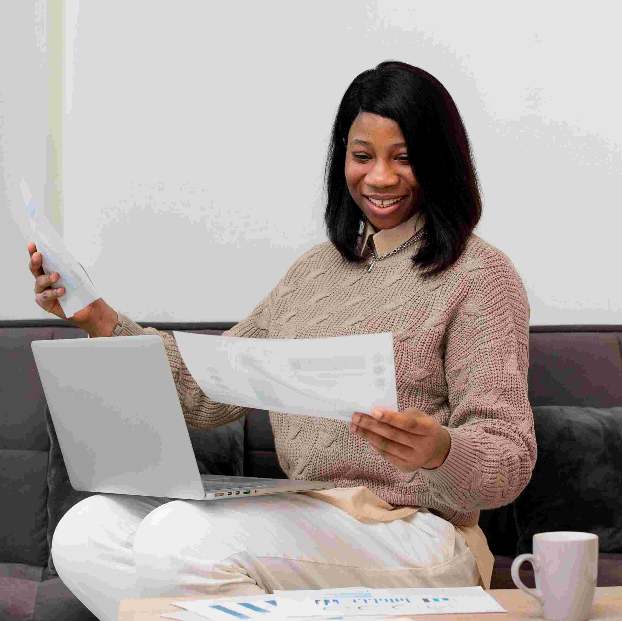a woman with her laptop on her lap while looking at a document - File Tax in Nigeria - BizEdge blog