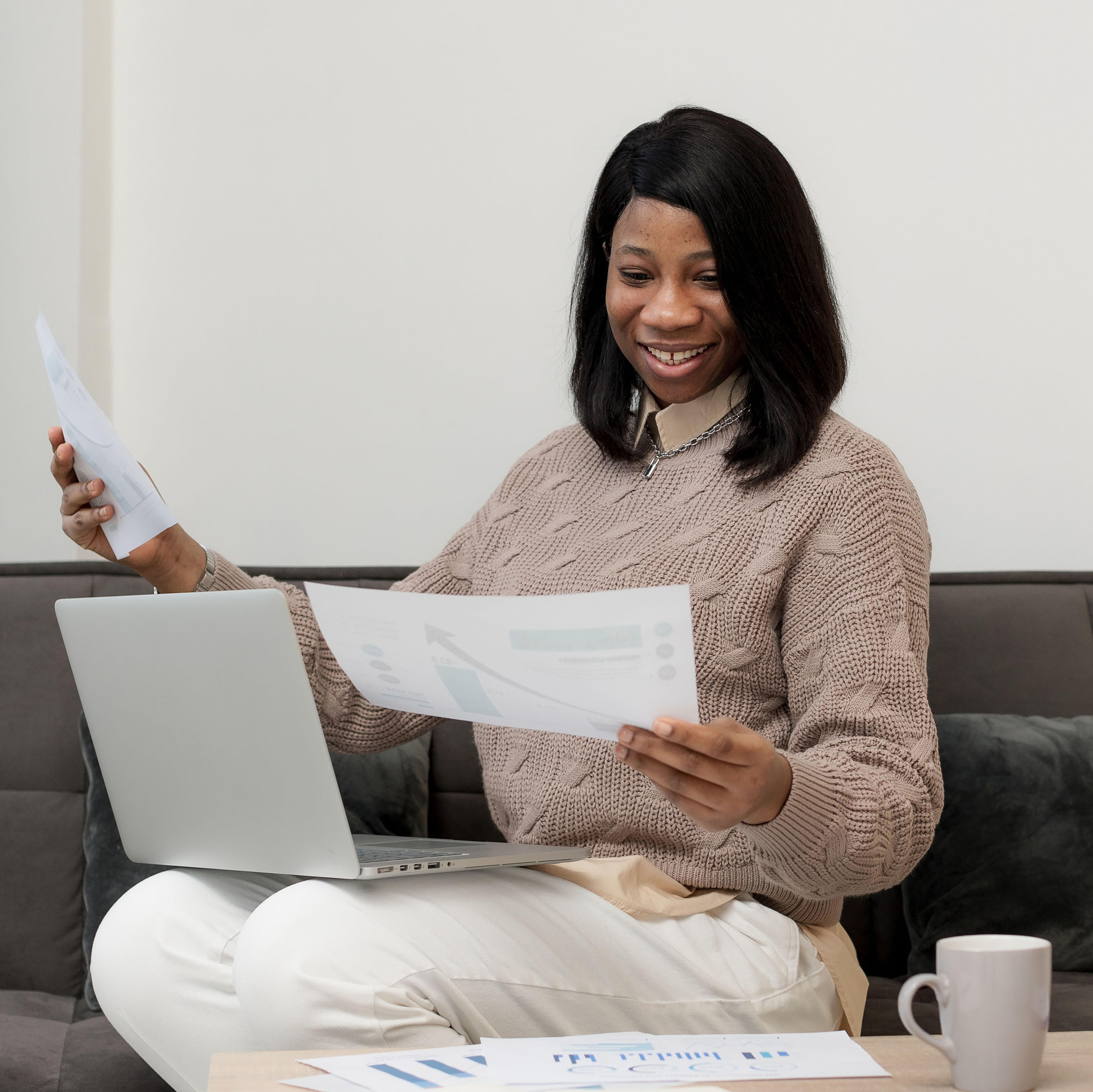 a woman with her laptop on her lap while looking at a document - File Tax in Nigeria - BizEdge blog