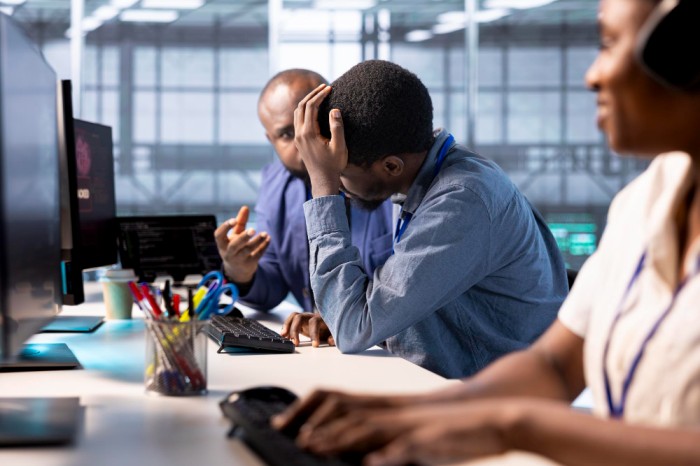 Team members working on a desk with one of them looking worried - Bad Organisational Experience - BizEdge blog