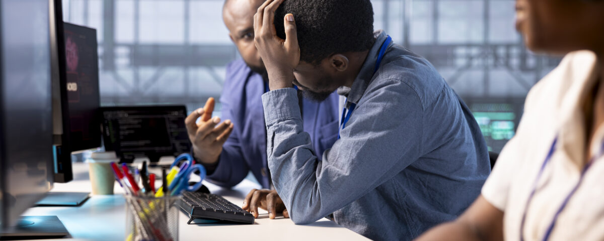 Team members working on a desk with one of them looking worried - Bad Organisational Experience - BizEdge blog