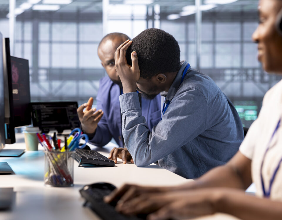 Team members working on a desk with one of them looking worried - Bad Organisational Experience - BizEdge blog