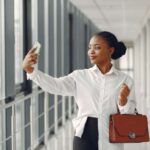 Black woman standing outside the office with a laptop bag taking pictures - Leave management system in Nigeria - BizEdge blog