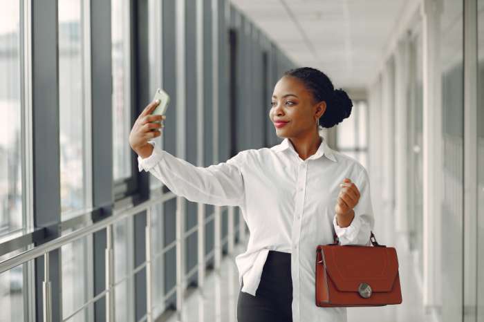 Black woman standing outside the office with a laptop bag taking pictures - Leave management system in Nigeria - BizEdge blog