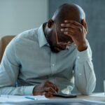 A man looking downcast while using a calculator - How Salary Advances Help Employees Beat Financial Stress