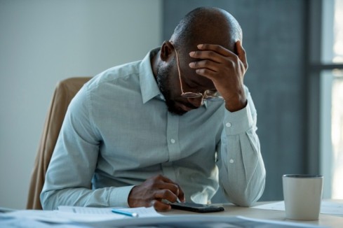 A man looking downcast while using a calculator - How Salary Advances Help Employees Beat Financial Stress